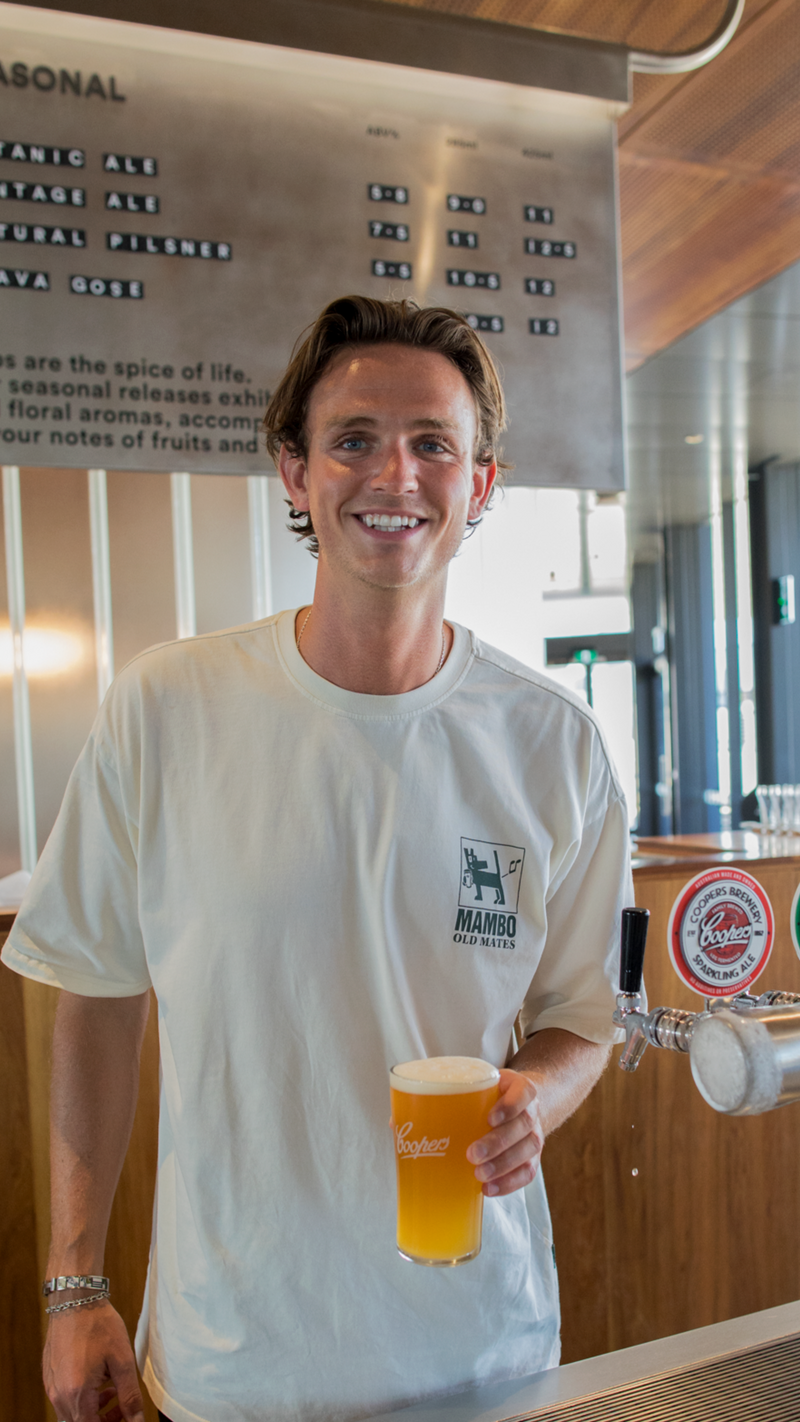 Man holding a beer at a bar with a menu board in the background